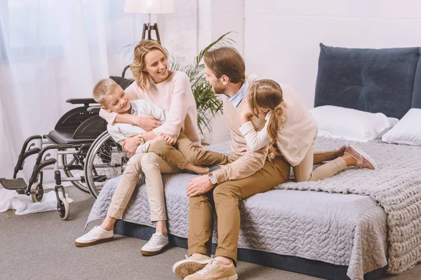 Père handicapé et mère heureuse assise avec des enfants au lit — Photo de stock