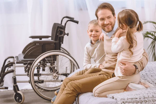 Happy father with disability sitting with children on bed — Stock Photo