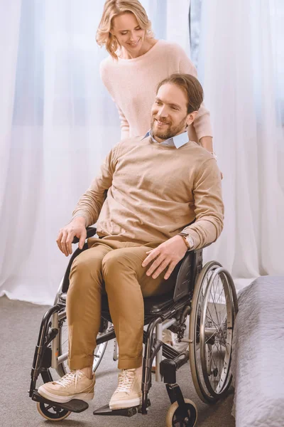 Esposa olhando para o marido sorridente na cadeira de rodas — Fotografia de Stock