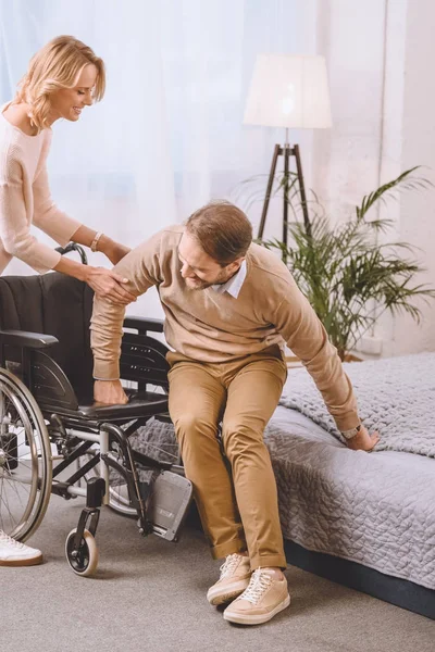 Wife helping husband with disability sit on wheelchair — Stock Photo