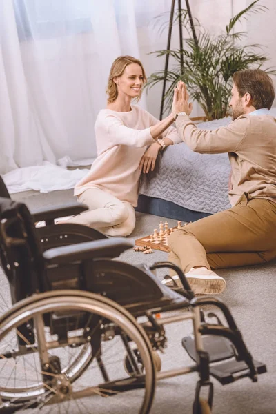 Mann mit Behinderung und Frau spielen Schach im Schlafzimmer und geben High Five — Stockfoto