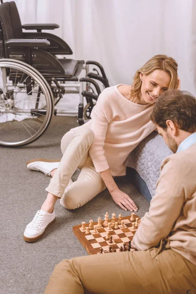 Marido con discapacidad y esposa feliz jugando ajedrez en el dormitorio - foto de stock