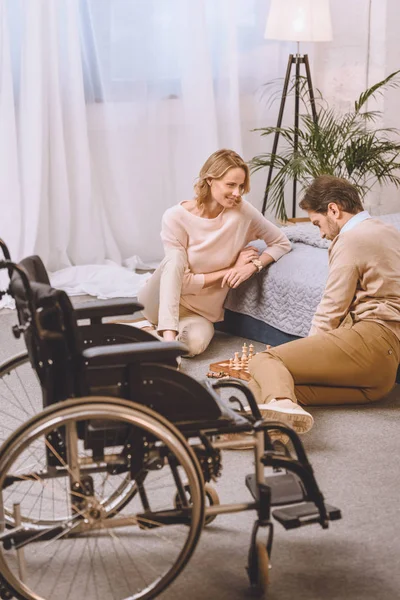 Marido con discapacidad y esposa jugando ajedrez en el dormitorio - foto de stock