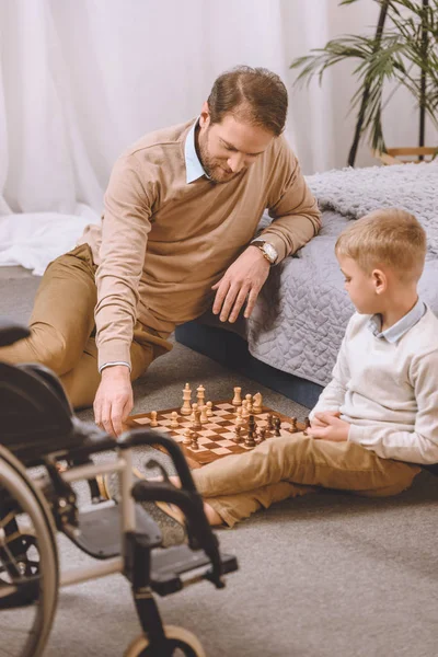 Father with disability and kid playing chess on floor — Stock Photo