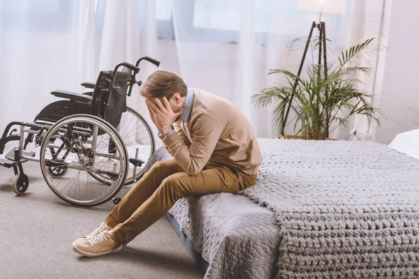 Upset man with disability sitting on bed and covering face with hands — Stock Photo
