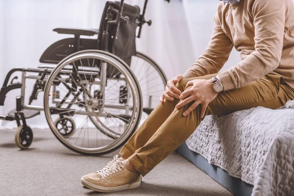 Cropped image of man with disability sitting on bed and touching legs — Stock Photo