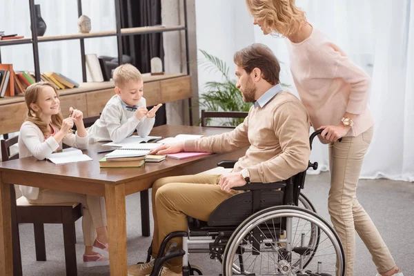 Padre sulla sedia a rotelle e madre che insegna ai bambini a casa — Foto stock