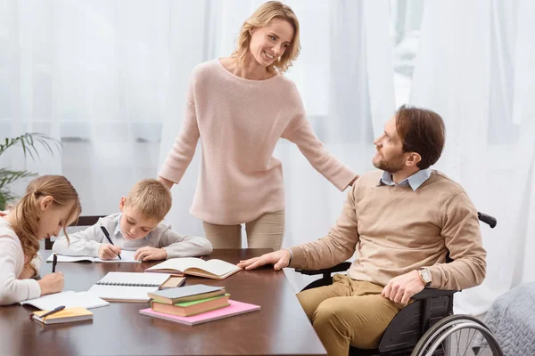 Padre feliz en silla de ruedas y madre enseñando a los niños en casa - foto de stock