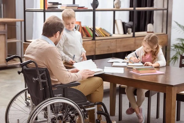 Padre en silla de ruedas ayudando a los niños con la educación en casa - foto de stock