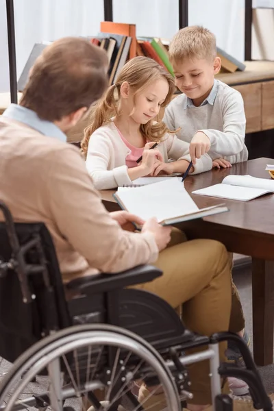 Father on wheelchair teaching kids at home — Stock Photo
