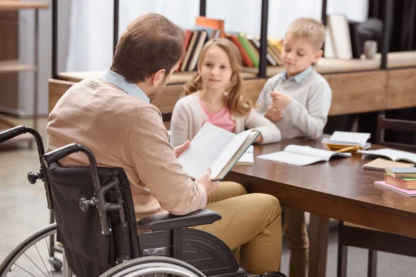 Father on wheelchair teaching children at home — Stock Photo