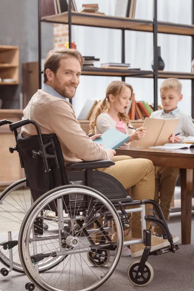 Отец на инвалидной коляске обучает детей дома и смотрит в камеру — стоковое фото