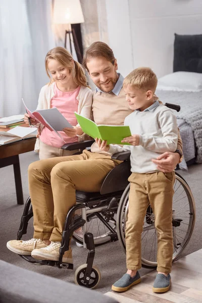 Happy father on wheelchair teaching children at home — Stock Photo