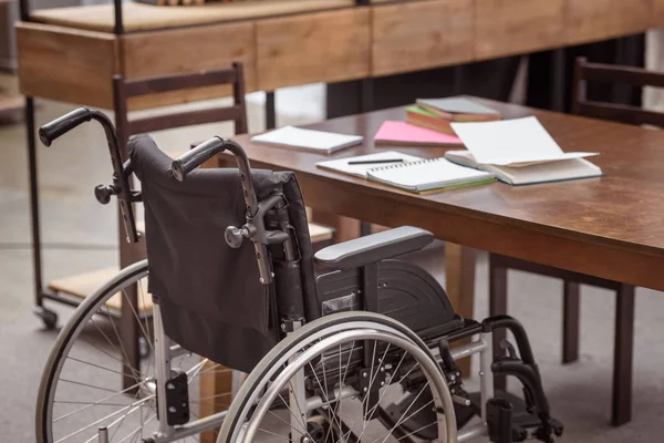 Leerer Rollstuhl am Tisch mit Notizbüchern — Stockfoto