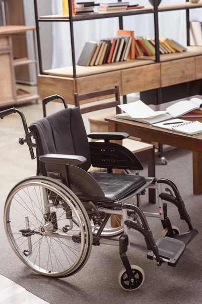 Cadeira de rodas vazia perto da mesa com cadernos no quarto — Fotografia de Stock