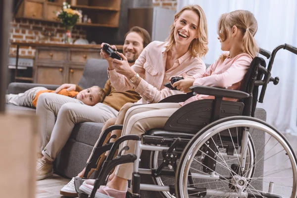 Famille avec enfant handicapé en fauteuil roulant jouant avec des joysticks ensemble à la maison — Photo de stock
