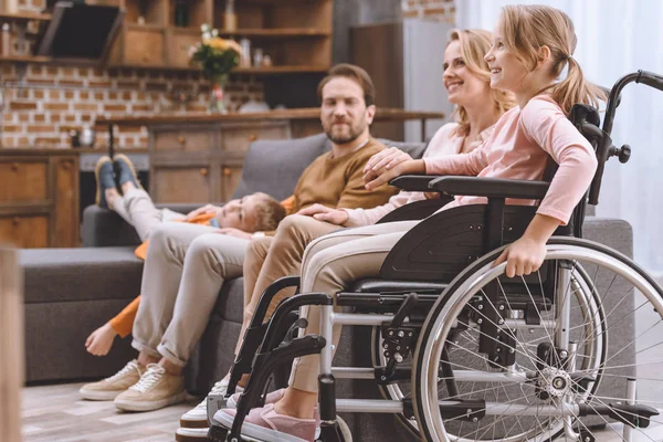 Счастливая семья с маленькой дочкой-инвалидом в инвалидной коляске проводит время вместе дома — стоковое фото