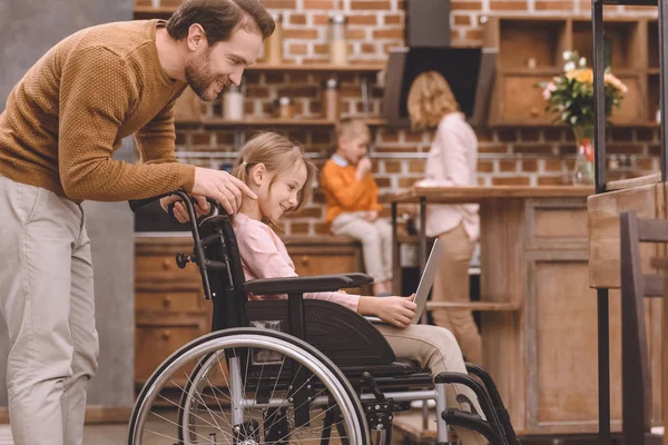 Seitenansicht eines glücklichen Vaters, der seine lächelnde behinderte Tochter zu Hause mit dem Laptop betrachtet — Stockfoto