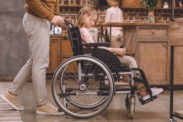 Ritagliato colpo di padre che trasporta sedia a rotelle con carina figlioletta utilizzando il computer portatile a casa — Foto stock