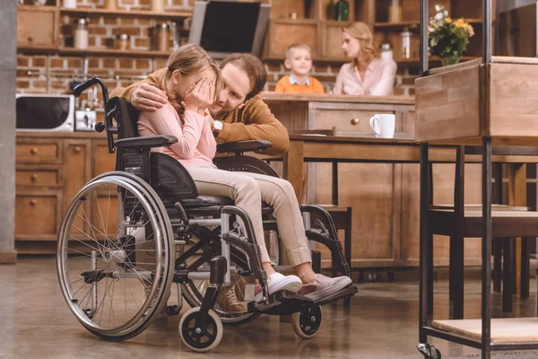 Vater umarmt kleine Tochter im Rollstuhl und schließt daheim die Augen mit den Händen — Stockfoto