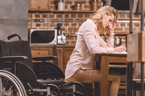 Vista lateral de la mujer discapacitada en silla de ruedas tomando notas mientras trabaja en casa — Stock Photo