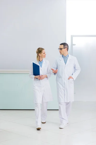 Two doctors in white coats with diagnosis talking in hospital corridor — Stock Photo