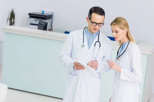 Two doctors in white coats with tablet discussing diagnosis in clinic — Stock Photo