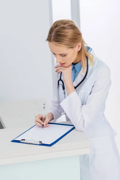 Feminino loira médico escrever diagnóstico no hospital — Fotografia de Stock