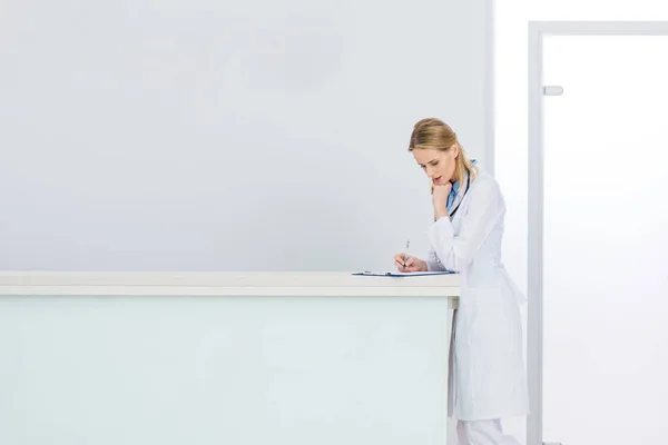 Femme médecin en manteau blanc écriture diagnostic à l'hôpital — Photo de stock