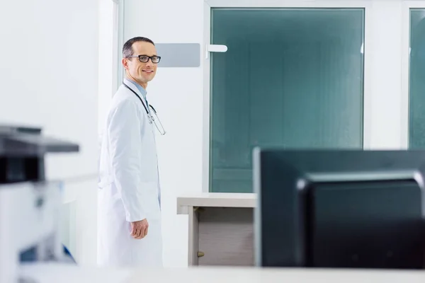 Medico maschio sorridente in mantello bianco con stetoscopio in ospedale — Foto stock
