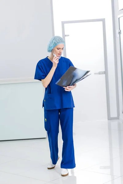 Female surgeon in medical cap and mask looking at x-ray in clinic — Stock Photo