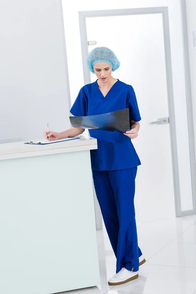 Female surgeon looking at x-ray and writing diagnosis in clinic — Stock Photo