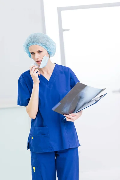 Cirurgiã feminina em boné médico e máscara segurando raio-X na clínica — Fotografia de Stock