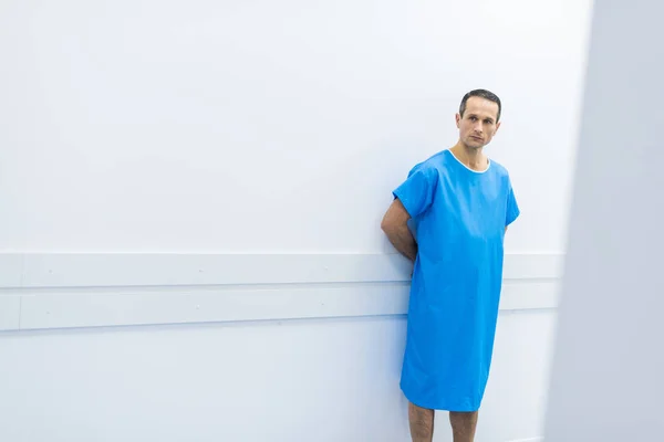 Paciente do sexo masculino em vestido médico em pé na parede do hospital — Fotografia de Stock
