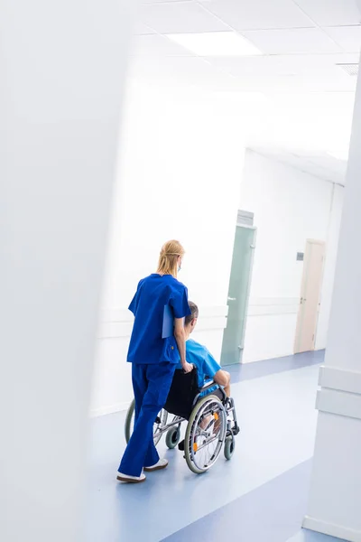 Вид сзади хирурга и расстроенный пациент в инвалидной коляске в коридоре больницы — стоковое фото