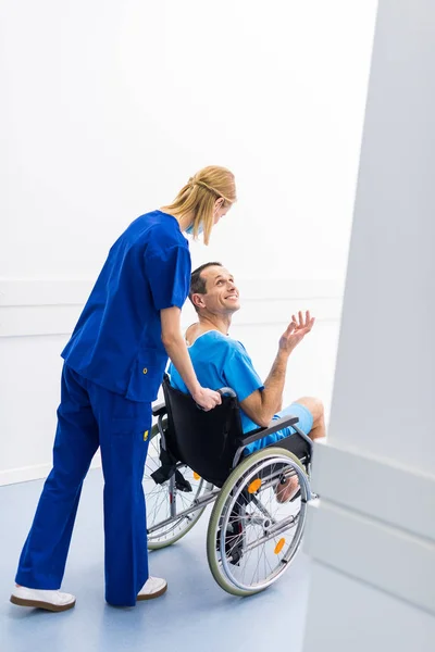 Chirurgo che parla con un paziente sorridente sulla sedia a rotelle nel corridoio dell'ospedale — Foto stock