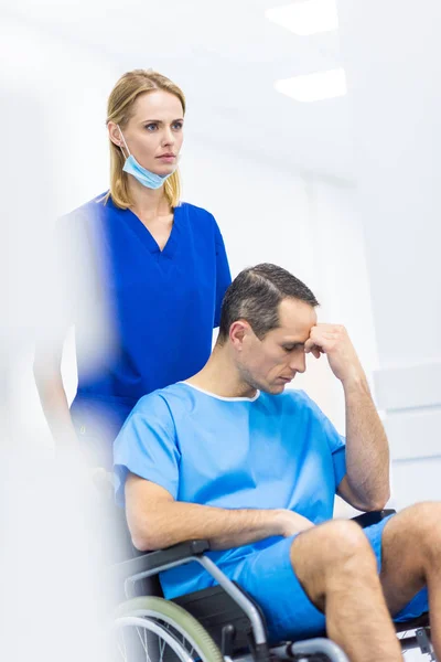 Surgeon and upset patient in wheelchair in hospital corridor — Stock Photo