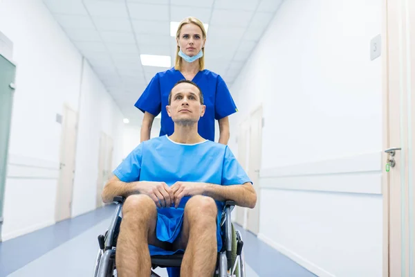 Female surgeon and male patient in wheelchair in hospital corridor — Stock Photo