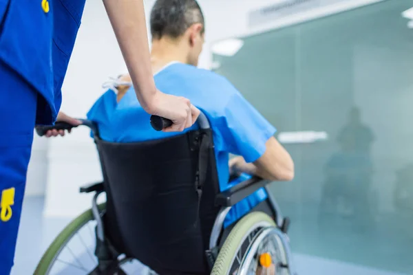 Vista trasera del cirujano y el paciente masculino en silla de ruedas en el pasillo del hospital - foto de stock