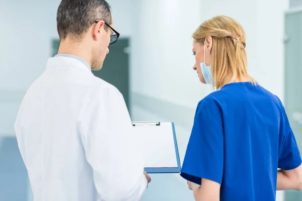 Vista posterior del médico en bata blanca y cirujana mujer discutiendo el diagnóstico en el hospital - foto de stock