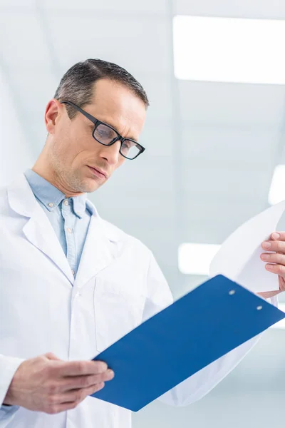 Male doctor in white coat reading diagnosis in hospital — Stock Photo