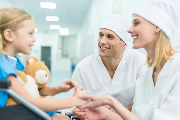Smiling doctors and patient on wheelchair holding hands — Stock Photo