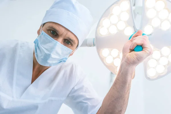 Vista inferior del médico de pie sobre el paciente en el quirófano y mirando a la cámara - foto de stock