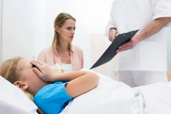 Kid covering face with hands while mother talking with doctor — Stock Photo