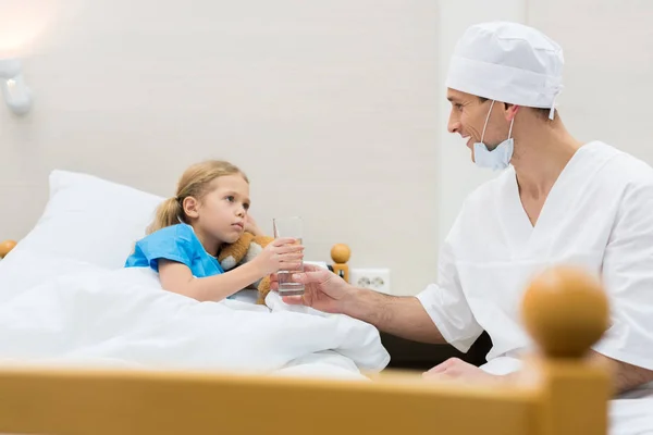 Medico sorridente dando bambino malato bicchiere d'acqua — Foto stock