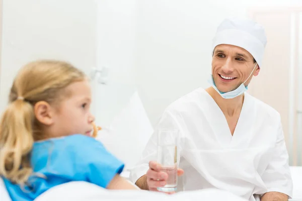 Médico sorrindo dando copo doente criança de água — Fotografia de Stock