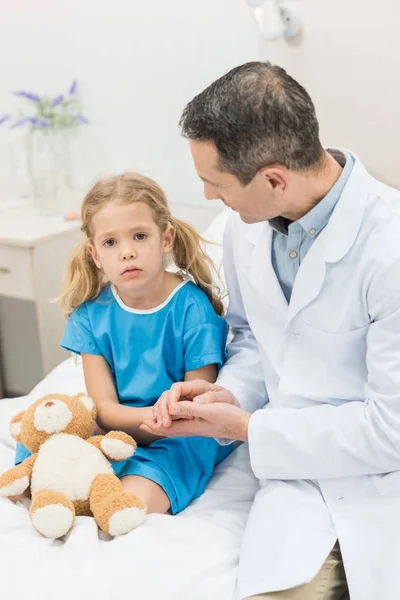 Male doctor holding hands with kid patient — Stock Photo