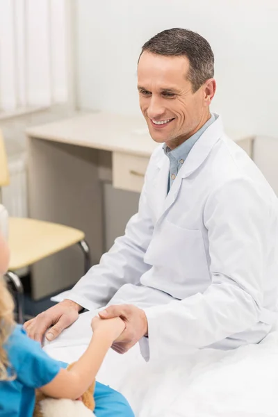 Sonriente médico cogido de la mano con niño paciente - foto de stock
