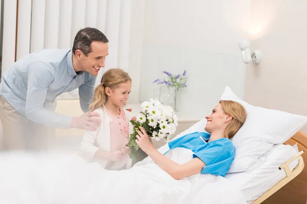 Happy father and daughter bringing flowers to sick woman — Stock Photo