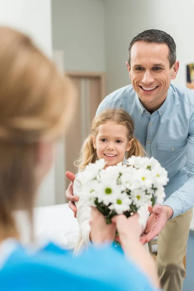 Smiling father and daughter bringing flowers to sick woman — Stock Photo